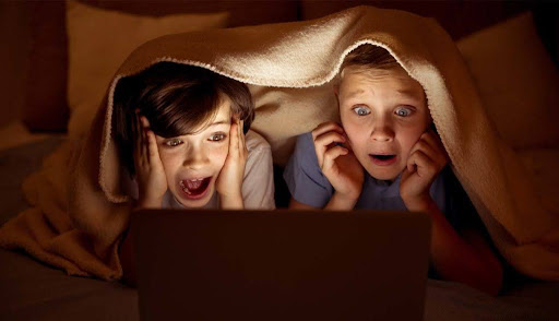 Two children watching a scary movie together, under a blanket